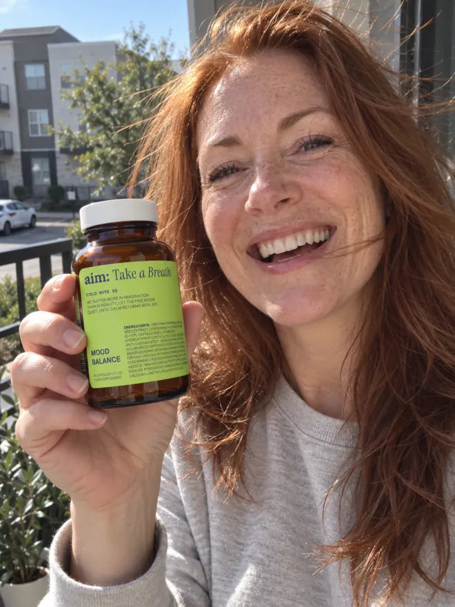 Someone on a balcony holding a bottle of AIM Mood Balance